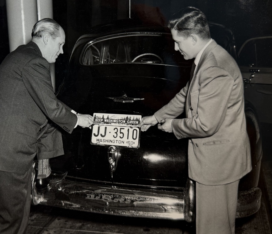 Washington Governor Arthur B Langlie applying a Keep Washington Green license plate topper to his car