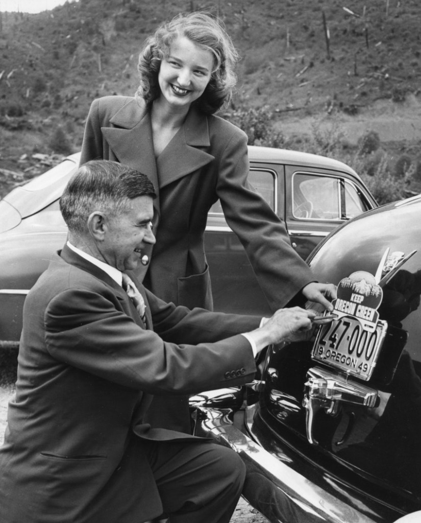 Promotional photo of Governor Douglas McKay attaching a Keep Oregon Green license plate topper to his car